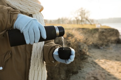 Woman pouring hot drink into cup from thermos outdoors, closeup