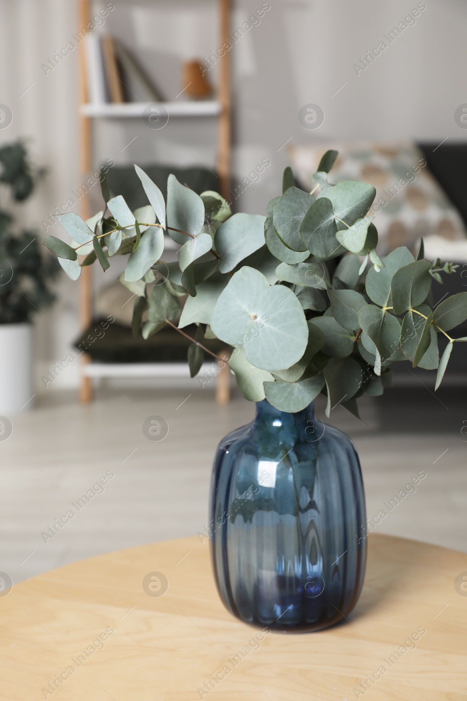 Photo of Blue glass vase with beautiful eucalyptus branches on wooden table in living room