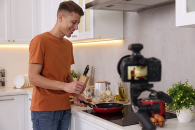 Smiling food blogger cooking while recording video in kitchen