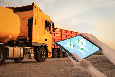 Logistics concept. Woman using tablet with world map on screen against trucks