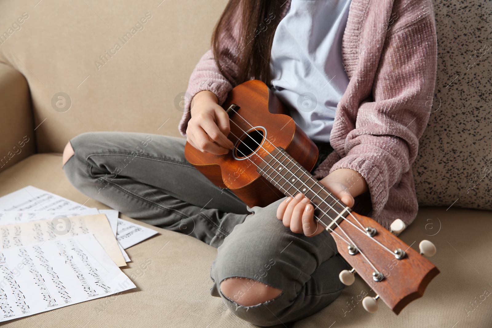 Photo of Little girl playing guitar on sofa, closeup