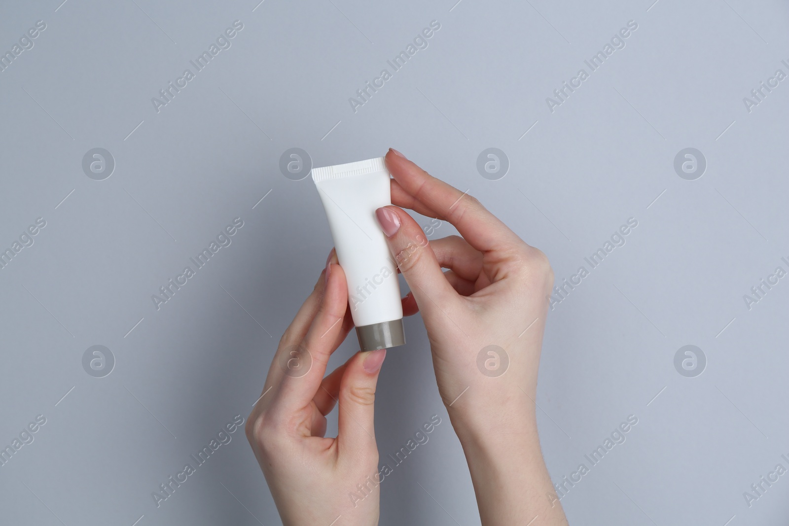 Photo of Woman holding tube of cream on grey background, closeup