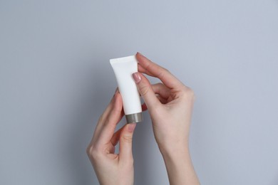 Woman holding tube of cream on grey background, closeup