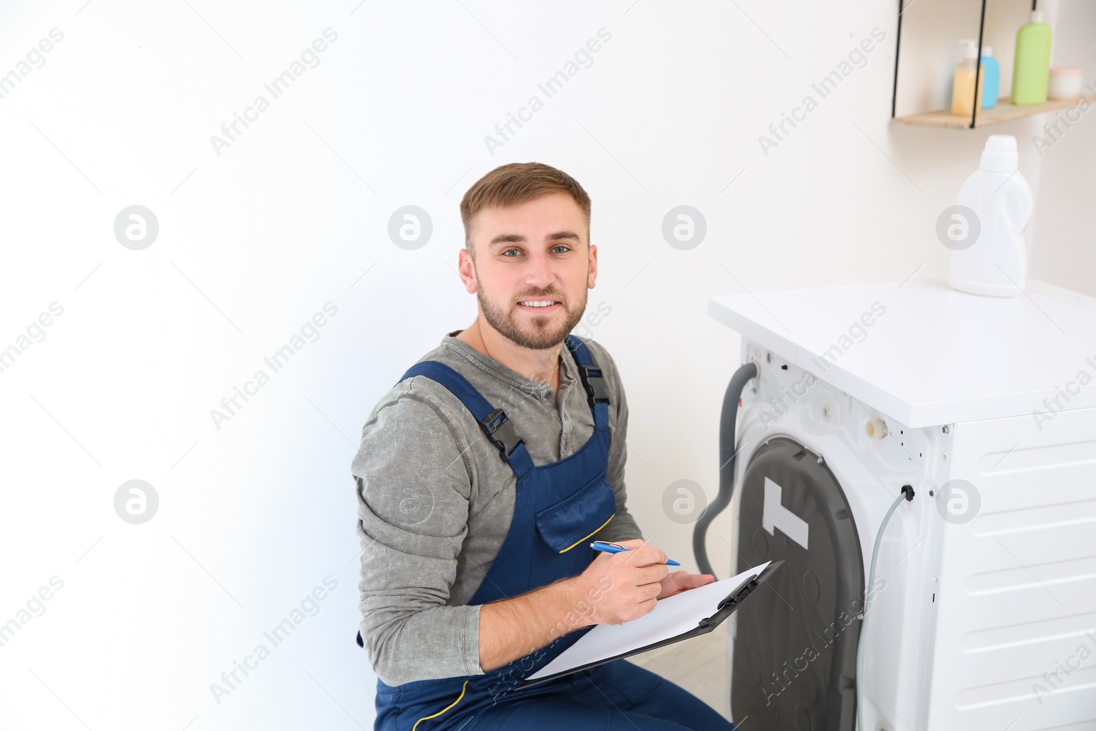 Photo of Young plumber with clipboard near washing machine in bathroom