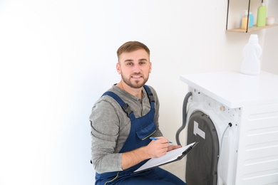 Young plumber with clipboard near washing machine in bathroom