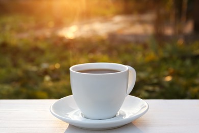 Photo of White cup with coffee on wooden table in morning outdoors