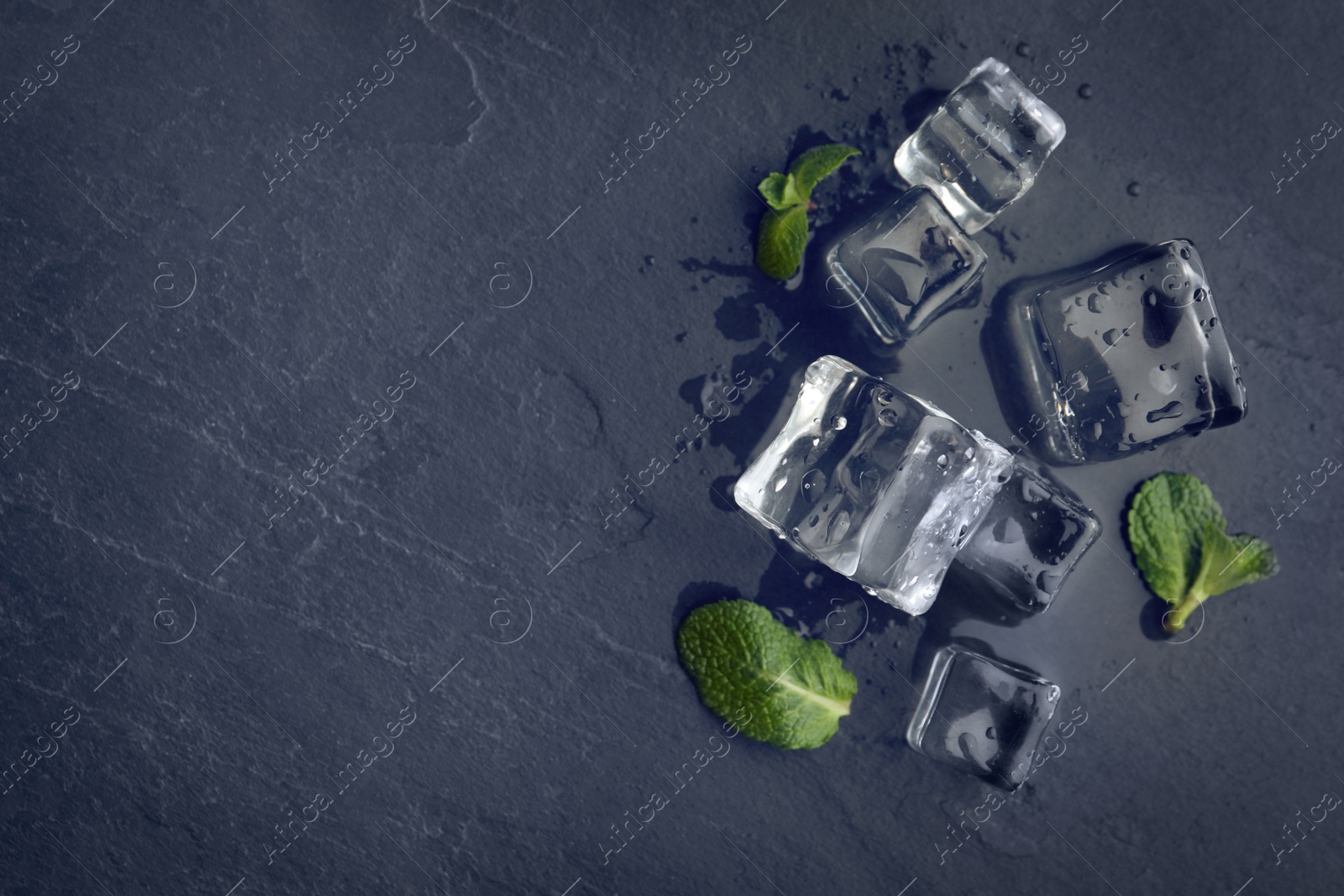 Photo of Crystal clear ice cubes with water drops and mint on black table, flat lay. Space for text