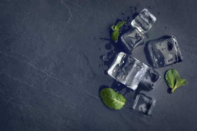 Photo of Crystal clear ice cubes with water drops and mint on black table, flat lay. Space for text