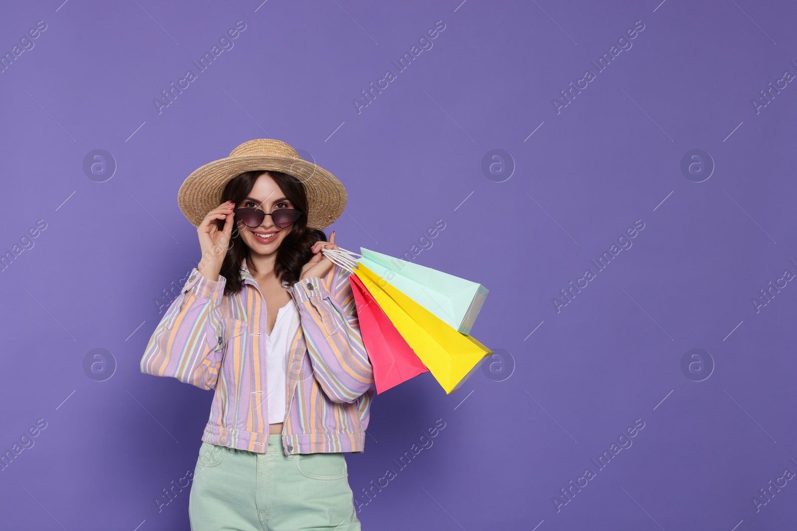 Photo of Beautiful young woman with paper shopping bags on purple background. Space for text