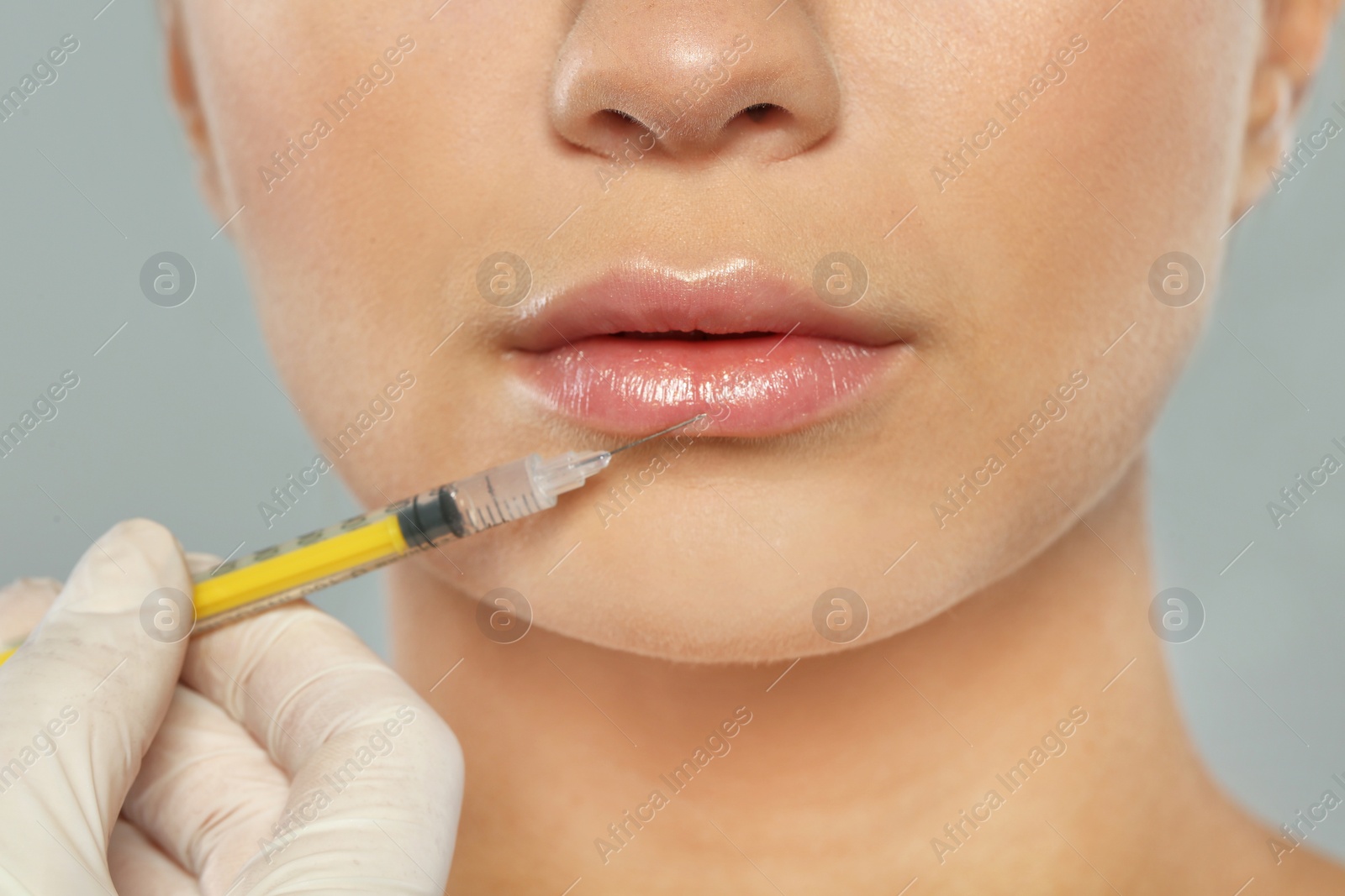 Photo of Young woman getting lips injection on grey background, closeup. Cosmetic surgery