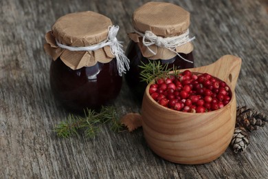 Tasty lingonberry jam in jars and cup with red berries on wooden table