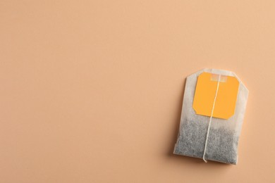 Photo of New tea bag with tab on pale orange background, top view. Space for text