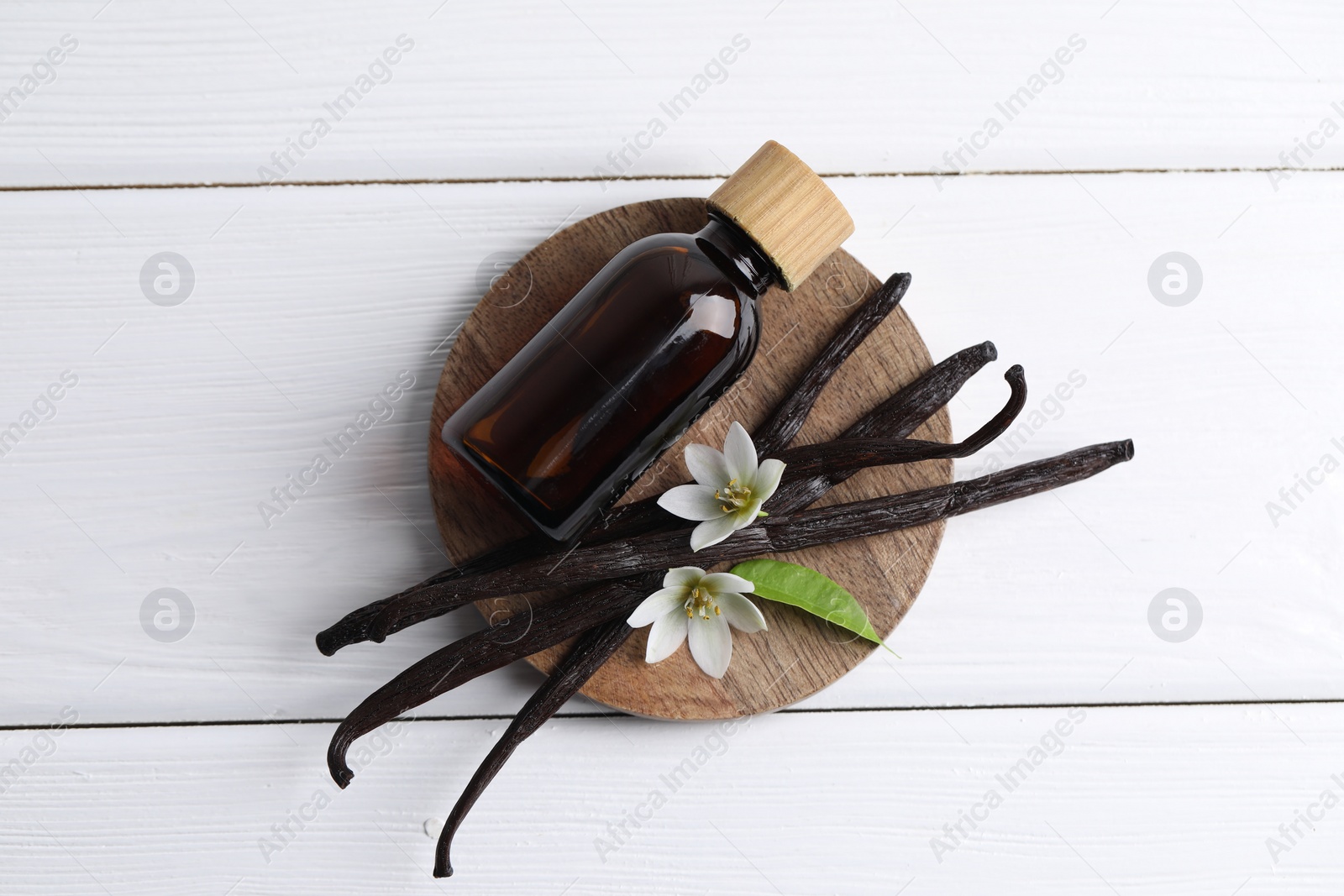 Photo of Vanilla pods, flowers, leaf and bottle with essential oil on white wooden table, top view