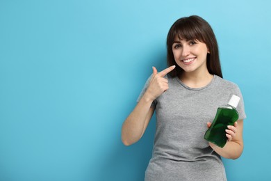 Photo of Young woman with mouthwash pointing at healthy teeth on light blue background, space for text