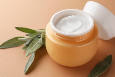 Photo of Jar of face cream and sage leaves on beige background, closeup