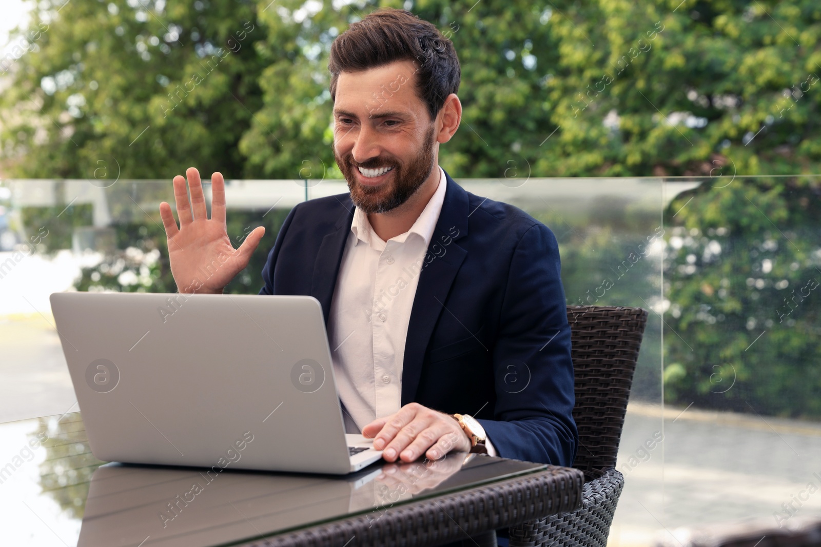 Photo of Happy bearded man having video chat in cafe outdoors