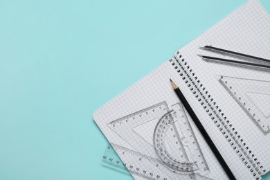 Photo of Different rulers, pencil, compass and notebook on turquoise background, flat lay. Space for text