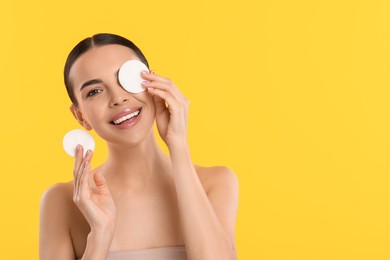 Photo of Beautiful woman removing makeup with cotton pads on yellow background, space for text