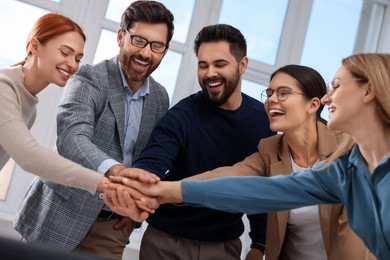 Photo of Team of employees joining hands in office
