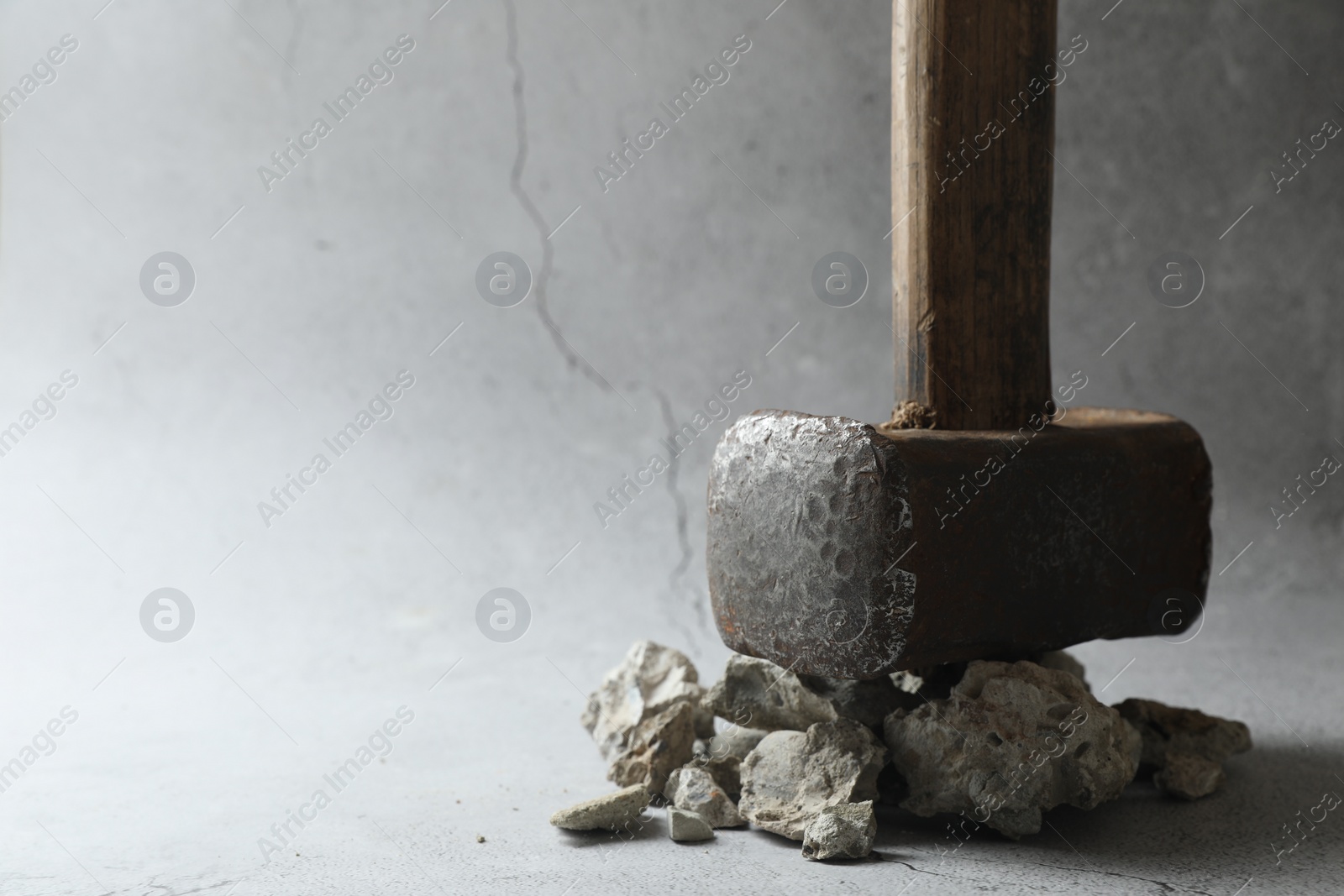 Photo of One sledgehammer and pieces of broken stones on grey background, closeup. Space for text