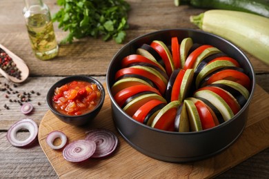 Photo of Cooking delicious ratatouille. Different fresh vegetables, and round baking pan on wooden table