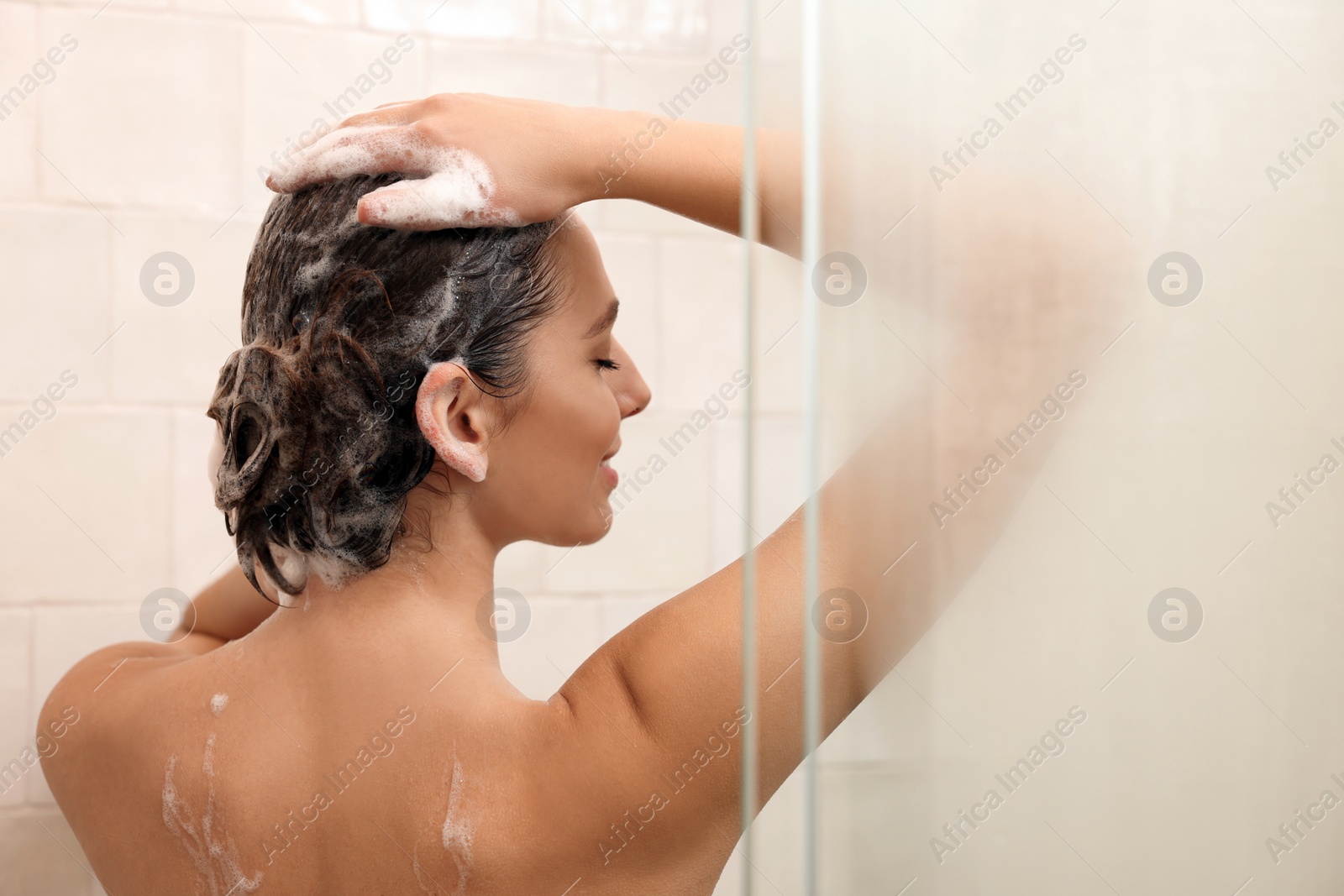 Photo of Young woman washing hair while taking shower at home