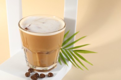 Photo of Refreshing iced coffee with milk in glass and beans on pale yellow background, space for text