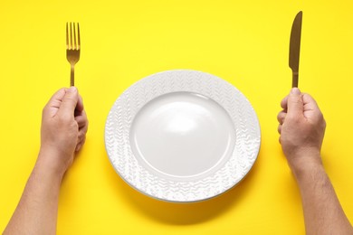 Photo of Man with fork, knife and empty plate at yellow table, closeup
