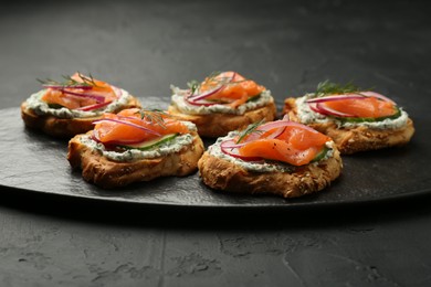 Photo of Tasty canapes with salmon, cucumber, radish and cream cheese on black table