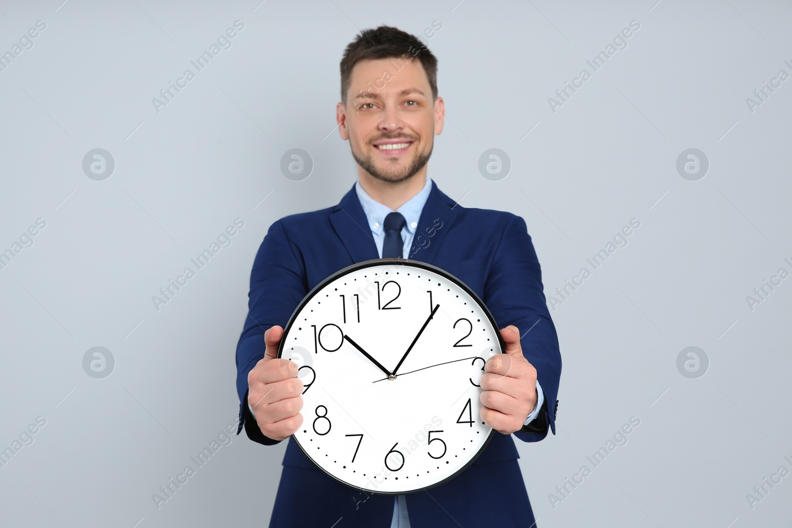 Photo of Happy businessman holding clock on grey background. Time management