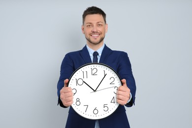 Happy businessman holding clock on grey background. Time management