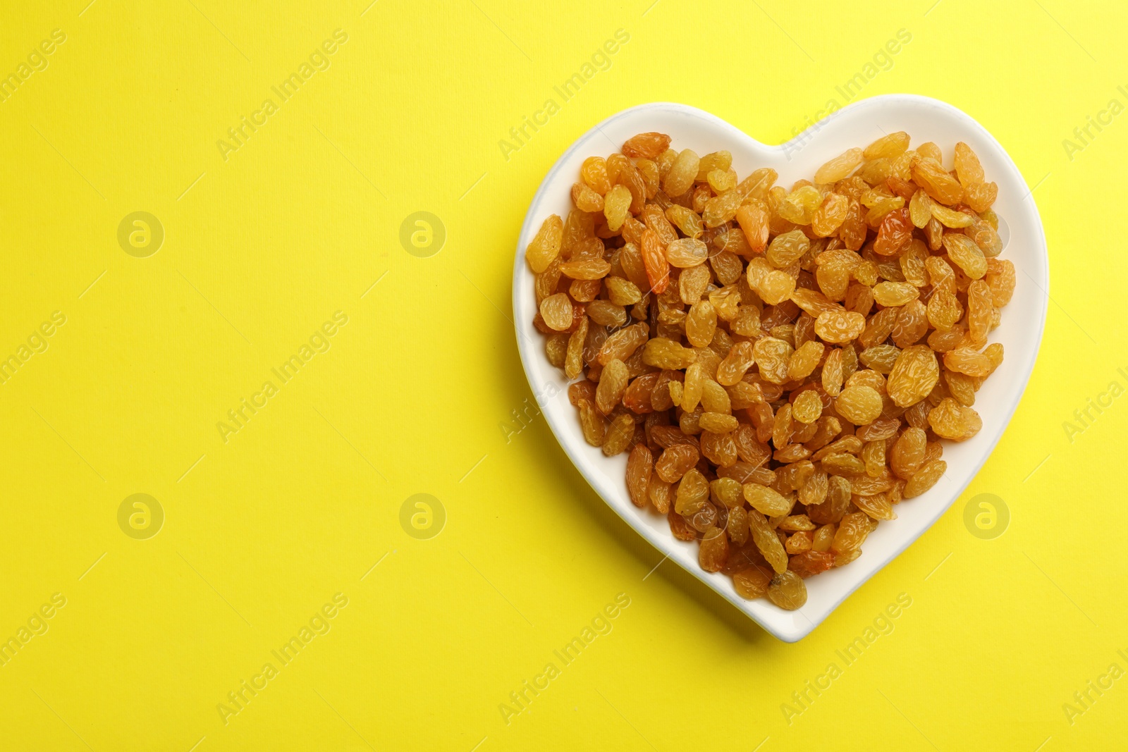 Photo of Heart shaped plate with raisins and space for text on color background, top view. Dried fruit as healthy snack