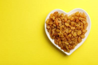 Photo of Heart shaped plate with raisins and space for text on color background, top view. Dried fruit as healthy snack