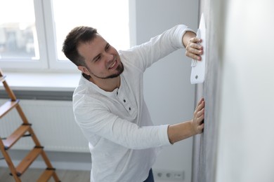 Photo of Man smoothing stylish gray wallpaper in room