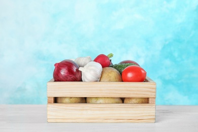 Photo of Wooden crate with ripe fruits and vegetables on white table against blue background. Space for text