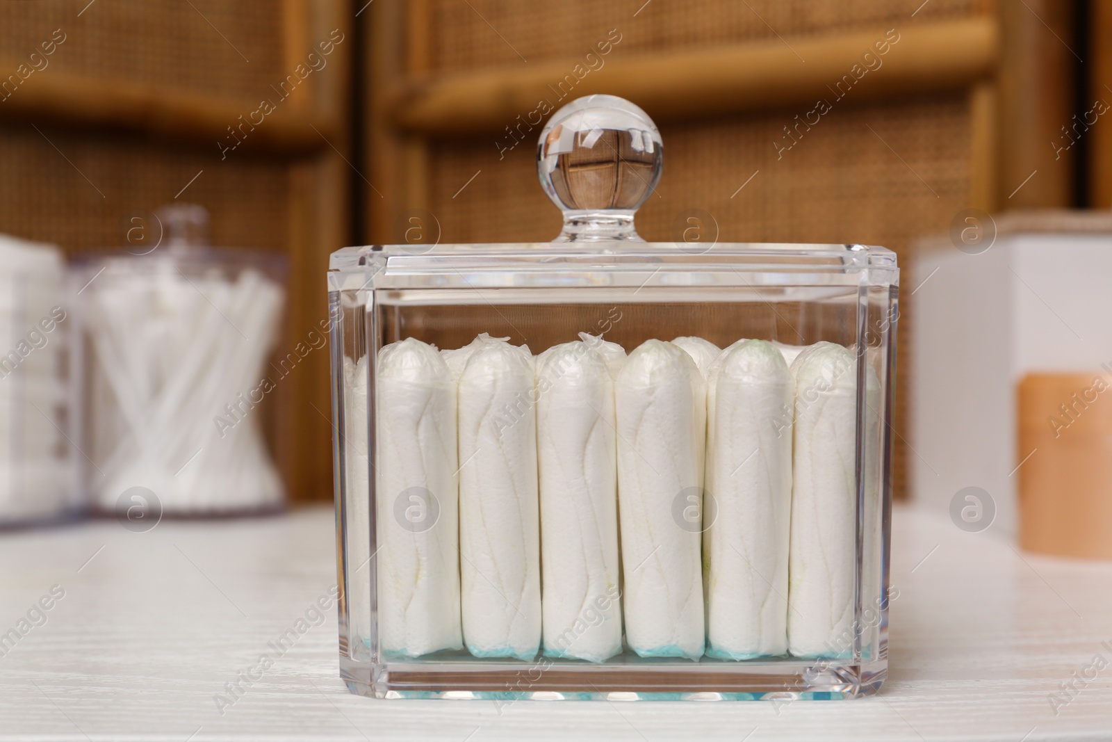 Photo of Glass holder with many tampons on white table. Menstrual hygienic product