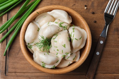 Photo of Bowl of tasty dumplings served on wooden board, flat lay