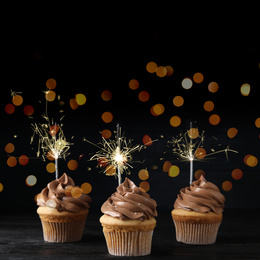 Birthday cupcakes with sparklers on wooden table against dark background