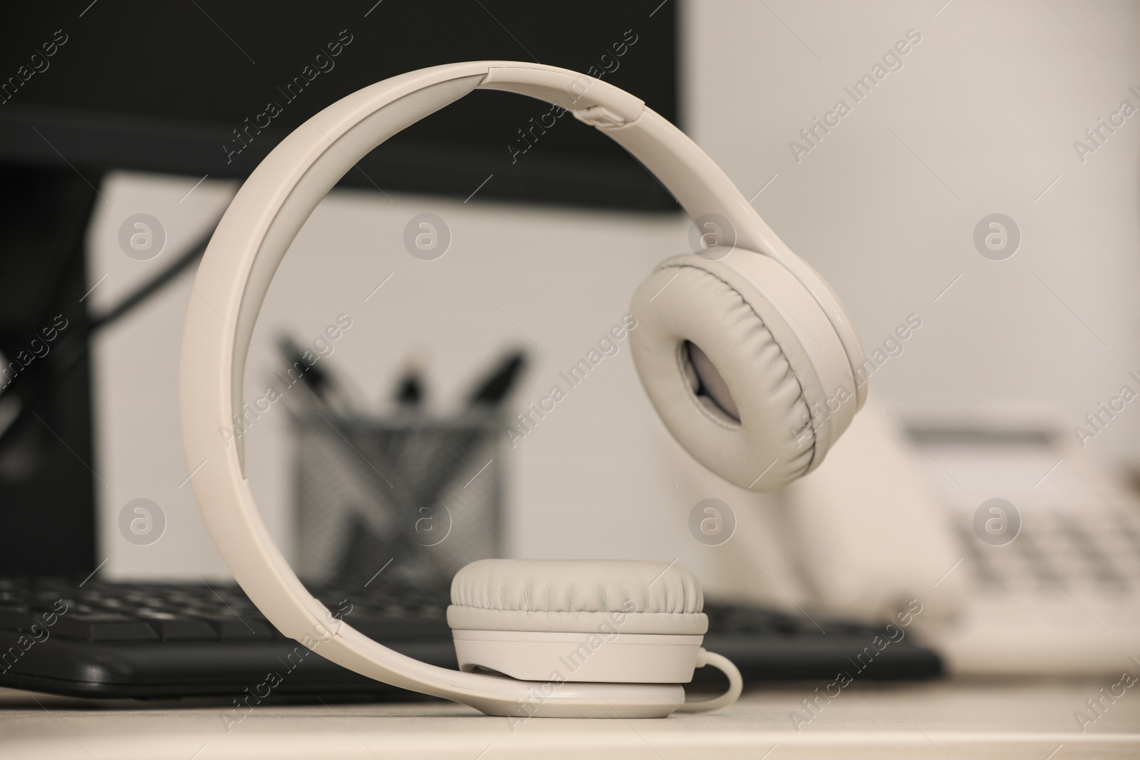 Photo of Modern headphones, desktop telephone and computer on table indoors