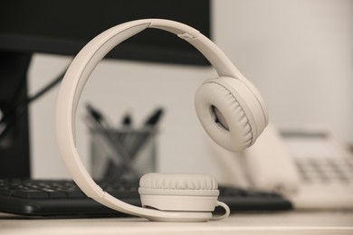 Photo of Modern headphones, desktop telephone and computer on table indoors