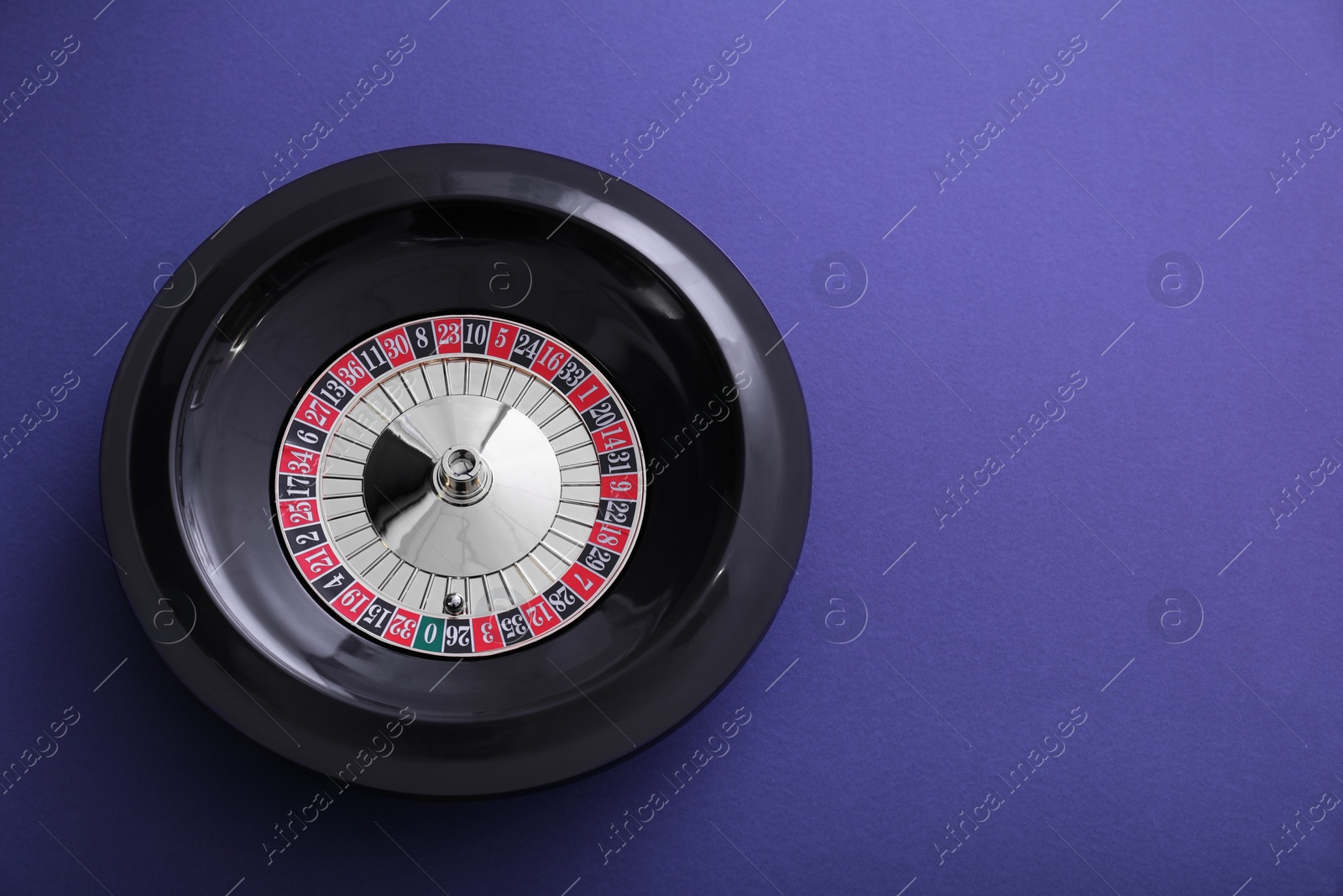 Photo of Roulette wheel with ball on dark violet background, top view and space for text. Casino game