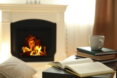 Photo of Cup of hot drink and book on table near fireplace at home. Cozy atmosphere