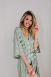 Photo of Pretty young woman in beautiful light green silk robe near white wall indoors