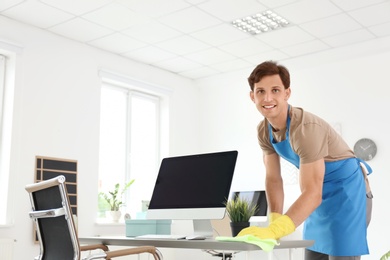 Photo of Young man in apron and gloves cleaning office