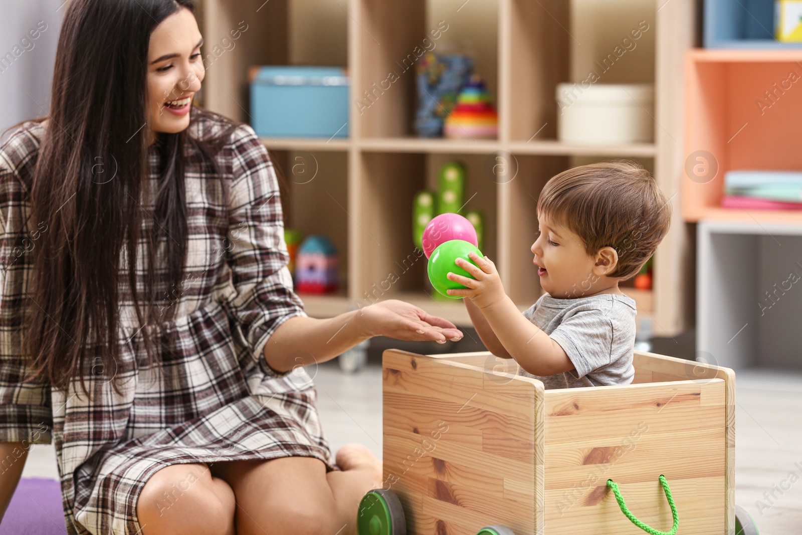 Photo of Young nanny and cute little baby playing with toys at home