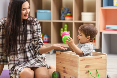 Photo of Young nanny and cute little baby playing with toys at home