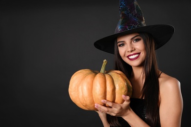 Photo of Beautiful woman wearing witch costume with pumpkin for Halloween party on black background, space for text