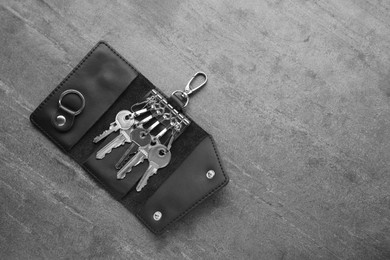Photo of Open leather holder with keys on grey table, top view. Space for text