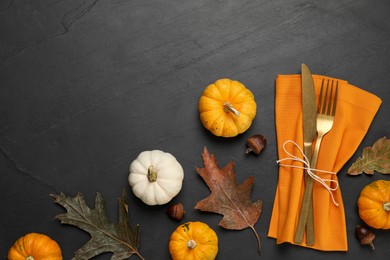 Photo of Cutlery, napkin and autumn decoration on black background, flat lay with space for text. Table setting