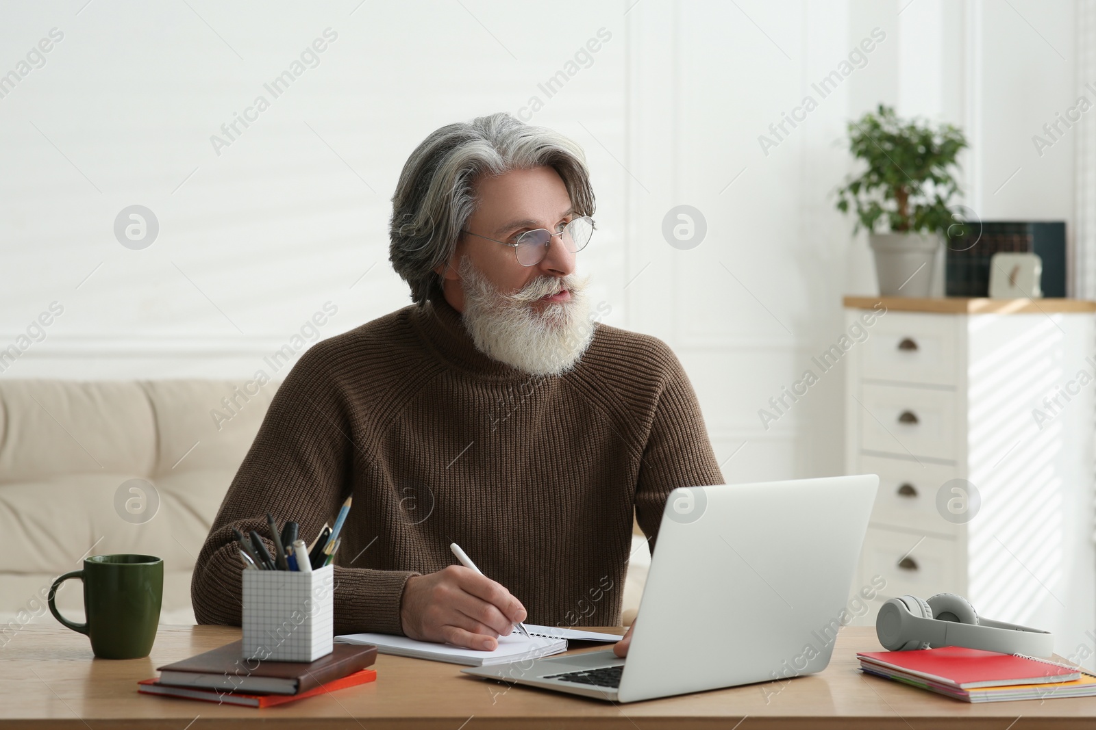 Photo of Middle aged man with laptop and notebook learning at table indoors